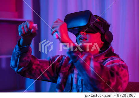 Young man wearing virtual reality (VR) glasses and uses joystick to play games with fun playing games in a room with red and blue lights, 3D game, Future games, Gadgets, Technology, Game concept Young man wearing virtual reality (VR) glasses and uses joystick to play games with fun playing games in a room with red and blue lights, 3D game, Future games, Gadgets, Technology, Game concept 97295863