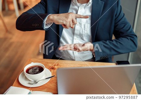 Businessman have a business meeting via video call and communicates using sign language in cafe Businessman have a business meeting via video call and communicates using sign language in cafe 97295887