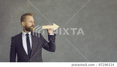 Serious businessman holding arrow and looking straight ahead on grey copy space background 97296314