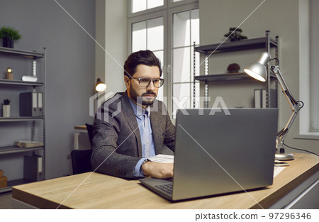 Focused confident businessman working on laptop in modern office Focused confident businessman working on laptop in modern office 97296346