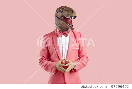 Funny man in a rubber dinosaur mask and a pink suit standing isolated on a pink background 97296402