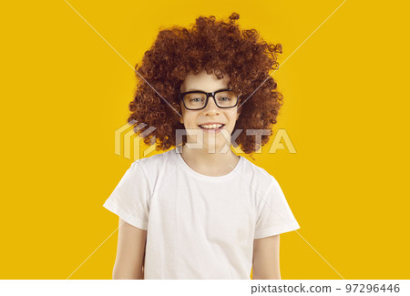 Happy child model in funny curly wig, T shirt and glasses isolated on orange background 97296446