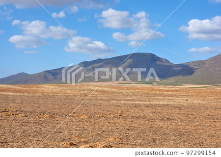 Farmland in the Western Cape of South Africa in the middle of the day. A mountain in a bare land with a cloudy blue sky. An empty farm with a nature view and a copy space. Farmland in the Western Cape of South Africa in the middle of the day. A mountain in a bare land with a cloudy blue sky. An empty farm with a nature view and a copy space. 97299154