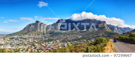 A mountain road overlooking the city with a cloudy blue sky. Panoramic landscape of green mountains surrounding an urban town and a scenic road for traveling along Cape Town, South Africa A mountain road overlooking the city with a cloudy blue sky. Panoramic landscape of green mountains surrounding an urban town and a scenic road for traveling along Cape Town, South Africa 97299667