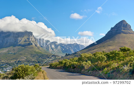 A road along a mountain and green nature with a cloudy blue sky and copy space. Beautiful landscape of a peaceful tarred roadway near plants and the wilderness on a summer day A road along a mountain and green nature with a cloudy blue sky and copy space. Beautiful landscape of a peaceful tarred roadway near plants and the wilderness on a summer day 97299702