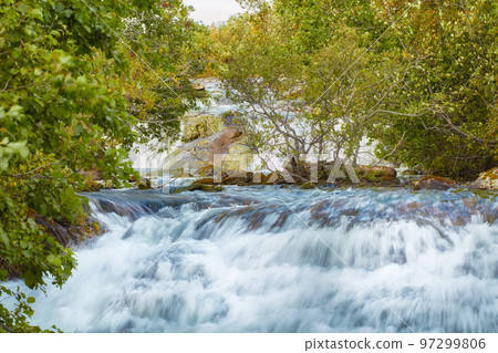 Closeup of a waterfall in the forest with green trees. Beautiful nature landscape of a natural rushing stream in a valley. Natural, fresh river flows between lush tree leaves in an eco environment 97299806