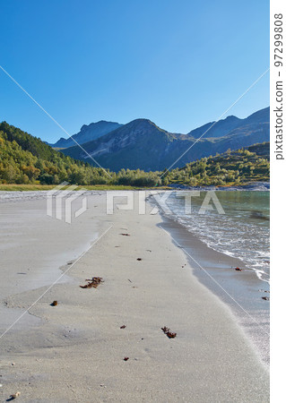 Sea and ocean view of beach waves washing onto empty and relaxing public seashore with forest and mountains background in Norway. Seascape with blue sky and copy space of calm, arctic and polar water 97299808