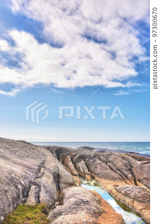 A rocky shore and a seascape view of the ocean with blue sky copy space and a mountain in the background in Camps Bay, Cape Town, South Africa. Calm, serene, tranquil beach and nature scenery A rocky shore and a seascape view of the ocean with blue sky copy space and a mountain in the background in Camps Bay, Cape Town, South Africa. Calm, serene, tranquil beach and nature scenery 97300670