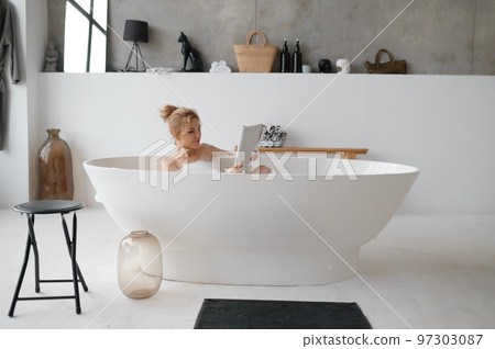 Beautiful young woman reading book or fashion magazine in bathtub Beautiful young woman reading book or fashion magazine in bathtub 97303087