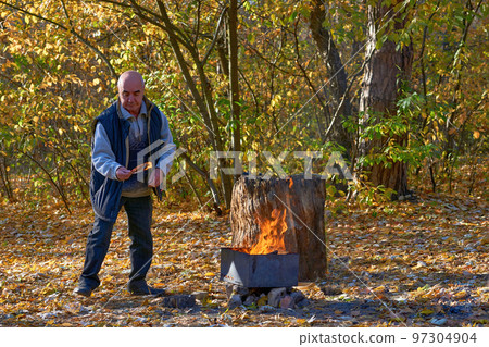 Cheerful elderly man pensioner makes a fire for grilling at a picnic in autumn Cheerful elderly man pensioner makes a fire for grilling at a picnic in autumn 97304904