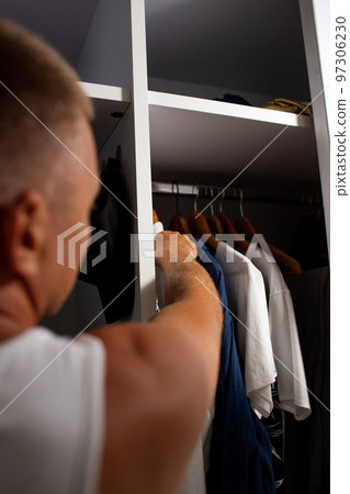 man hangs his shirt in the closet 97306230
