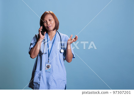 Elderly specialist nurse in medical coat talking at phone with remote practitioner discussing medication treatment. Cheerful assistant explaining patient diagnosis, medicine concept and service Elderly specialist nurse in medical coat talking at phone with remote practitioner discussing medication treatment. Cheerful assistant explaining patient diagnosis, medicine concept and service 97307201