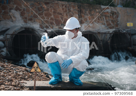 Ecologist sampling water toxic chemicals from river with test tube glass and have white smoke, Biologist wear protective suit and mask collects sample waste water from industrial, problem environment Ecologist sampling water toxic chemicals from river with test tube glass and have white smoke, Biologist wear protective suit and mask collects sample waste water from industrial, problem environment 97309568