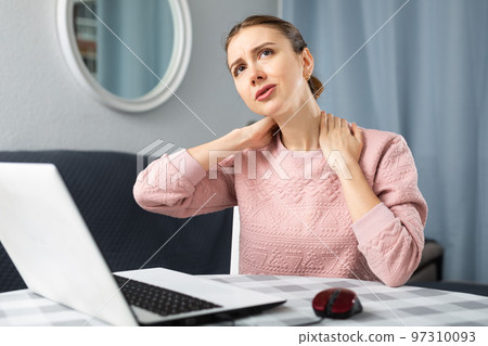 Woman feeling pain in neck while working at home 97310093