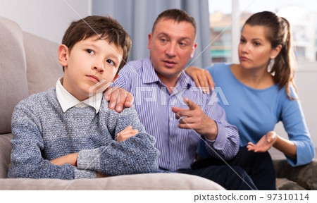 Frowning boy with mother and father berating him 97310114