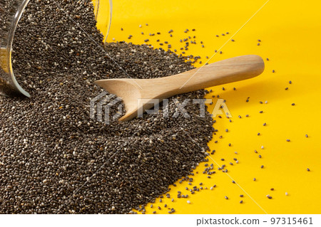 Healthy breakfast, Chia seeds are pouring out from glass jar with wood spoon over yellow background Healthy breakfast, Chia seeds are pouring out from glass jar with wood spoon over yellow background 97315461