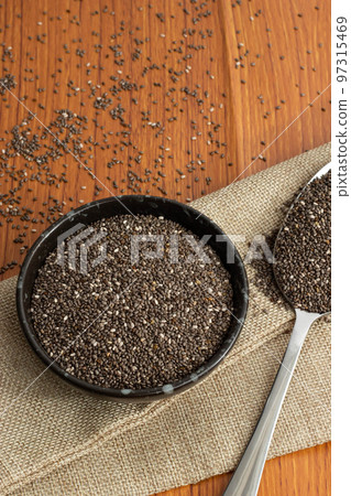 Healthy breakfast, Chia seeds in black bowl and superfood in spoon falling on wooden background Healthy breakfast, Chia seeds in black bowl and superfood in spoon falling on wooden background 97315469