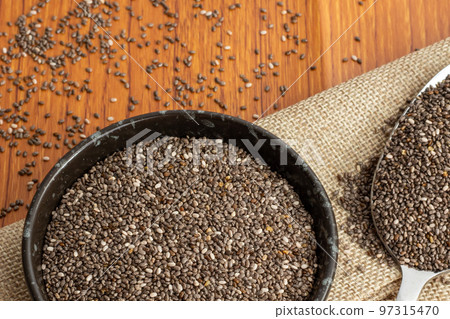 Healthy breakfast, Chia seeds in black bowl and superfood in spoon falling on wooden background Healthy breakfast, Chia seeds in black bowl and superfood in spoon falling on wooden background 97315470
