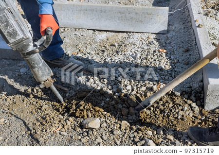Construction workers using jackhammer to dig out concrete surface on side of road 97315719