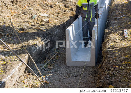 Installation of precast concrete u-shaped drains on reconstruction road as part drainage road work Installation of precast concrete u-shaped drains on reconstruction road as part drainage road work 97315757