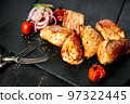 Close-up appetizing pork shish kebab on a black stone cutting board. Red onion, cherry tomatoes and two forks. Soft focus. Copy space 97322445