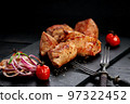 Appetizing pork shish kebab on a black stone cutting board. Red onion, cherry tomatoes and two forks. Soft focus 97322452