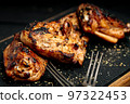 Close-up appetizing BBQ chicken thighs on a black cutting board. Soft focus. 97322453