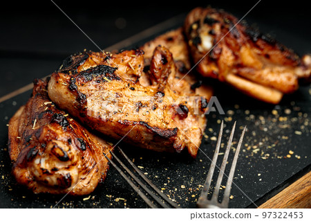 Close-up appetizing BBQ chicken thighs on a black cutting board. Soft focus. 97322453