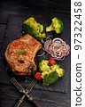 Appetizing BBQ pork loin with vegetables on a black stone board. Roast pork and broccoli. Vertical shot. Copy space. Old rustic wooden background 97322458