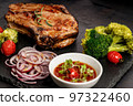 Close-up BBQ pork loin with spicy sauce and vegetables on a black stone board. Selective focus. Old rustic wooden background 97322460