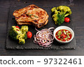 Delicious BBQ Pork Loin with spicy sauce and vegetables on a black stone board. Top view. Old rustic wooden background 97322461