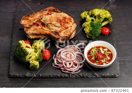 Delicious BBQ Pork Loin with spicy sauce and vegetables on a black stone board. Top view. Old rustic wooden background 97322461