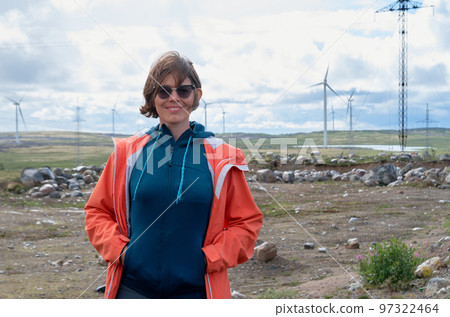 Smiling woman in orange jacket and sunglasses in front of wind farm 97322464