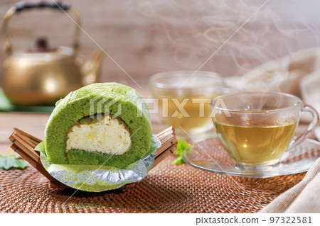 Matcha Green Tea Roll Cake with white cream inside and hot green tea in the cup background. Foods or dessert concept. 97322581