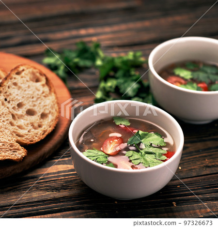 slice of bread and two plates of soup on a wooden board. 97326673