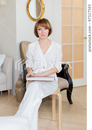 An adult beautiful woman spends time in her stylish living room and holds a big book in her hands. 97327565
