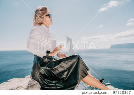 Digital nomad, Business woman working on laptop by the sea. Pretty lady typing on computer by the sea at sunset, makes a business transaction online from a distance. Freelance, remote work on vacation Digital nomad, Business woman working on laptop by the sea. Pretty lady typing on computer by the sea at sunset, makes a business transaction online from a distance. Freelance, remote work on vacation 97328397