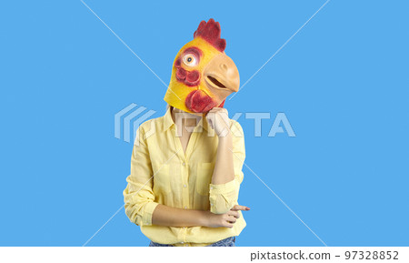 Funny woman in rubber mask of chicken posing in pensive pose on light blue background. 97328852