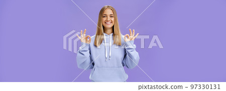 Girl got everything under control. Delighted happy charming woman with fair hair and tanned skin without makeup showing okay gesture smiling assured and pleased posing in hoodie over purple wall 97330131