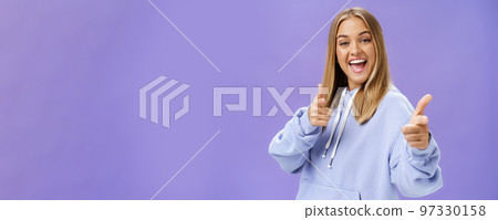 Enthusiastic and charismatic woman feeling joyful meeting friends checking out cool copy space pointing with finger guns at camera smiling broadly posing in stylish hoodie over purple wall Enthusiastic and charismatic woman feeling joyful meeting friends checking out cool copy space pointing with finger guns at camera smiling broadly posing in stylish hoodie over purple wall 97330158
