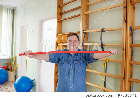 a young man with down syndrome is engaged in a gym with a gymnastic stick. rehabilitation process. 97330571