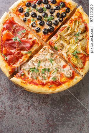 four seasons pizza quattro stagioni made with tomato sauce, mozzarella cheese, ham, artichokes, olives and mushrooms closeup on the board on the table. Vertical top view 97333109