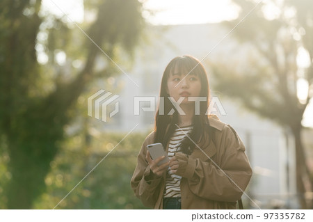 A young woman operating a smartphone outdoors A young woman operating a smartphone outdoors 97335782