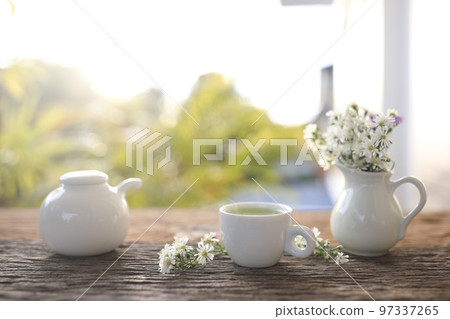 Tea cup and tea pot and aster flowers in white vase on wooden table  97337265
