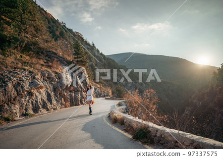 The woman is dear to the mountains. A woman in a white sweater, black boots and a hat walks along a winding alpine path between the mountains at the end of summer at sunset. Travel concept. 97337575