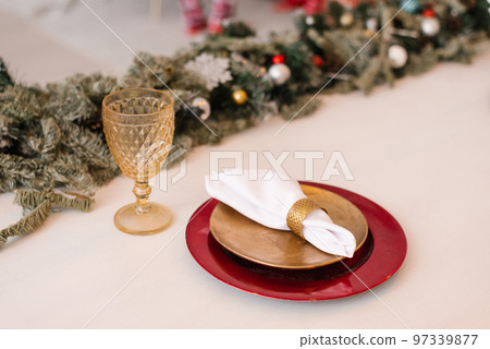 Traditional Christmas table setting. Burgundy and gold plate, linen napkin, fir branches and glass goblet. Festive dinner decor 97339877