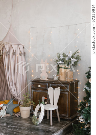 Interior of a children's room decorated for Christmas. Awning bed with toys and pillows, a tree, a wardrobe and an armchair in gray beige colors Interior of a children's room decorated for Christmas. Awning bed with toys and pillows, a tree, a wardrobe and an armchair in gray beige colors 97339914