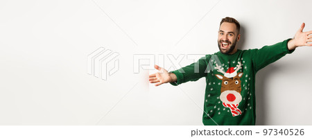 New year celebration and winter holidays concept. Friendly man spread hands for hug, welcome to Christmas party, wearing funny sweater, white background New year celebration and winter holidays concept. Friendly man spread hands for hug, welcome to Christmas party, wearing funny sweater, white background 97340526