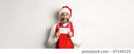Winter holidays and shopping concept. Excited handsome man planning new year, holding Christmas sock for gifts and thinking, standing over white background Winter holidays and shopping concept. Excited handsome man planning new year, holding Christmas sock for gifts and thinking, standing over white background 97340535