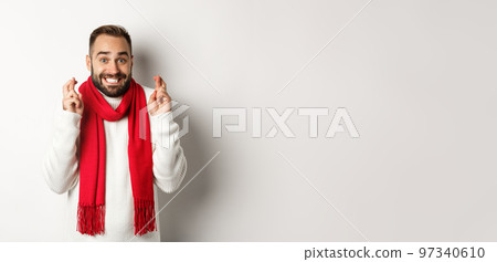 Christmas holidays and New Year concept. Hopeful man making wish with fingers crossed, waiting for gifts, standing over white background Christmas holidays and New Year concept. Hopeful man making wish with fingers crossed, waiting for gifts, standing over white background 97340610